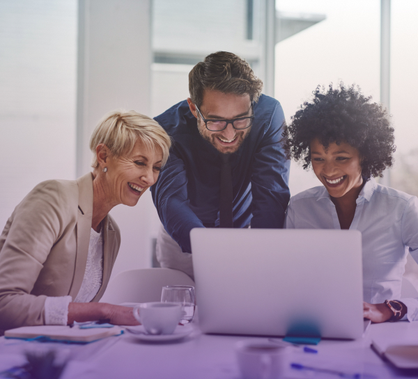 Três funcionários da Edge UOL em um escritório, onde todos sorriem enquanto olham a tela do notebook que está na mesa.